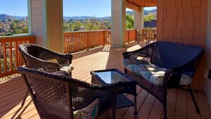 A covered outdoor deck with wicker furniture and a glass table, overlooking a scenic landscape. - Longview Lodge - Prescott Cabin Rentals (Prescott)