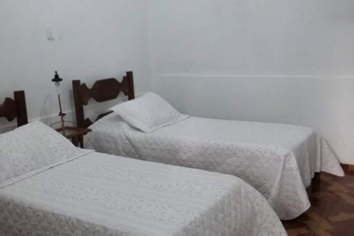Two single beds with wooden headboards and white linens in a room with plain walls and a tiled floor.