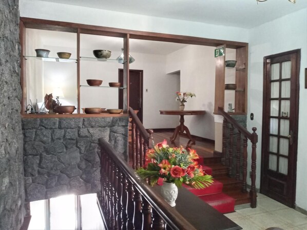 A staircase with a wooden handrail, a stone wall on one side, and a shelf with bowls and a lamp.