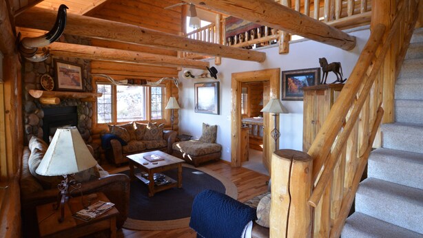 A log cabin interior with a fireplace, wooden staircase, and a cozy living area with furniture. - Lone Pine Lodge - Prescott Cabin Rentals (Prescott)