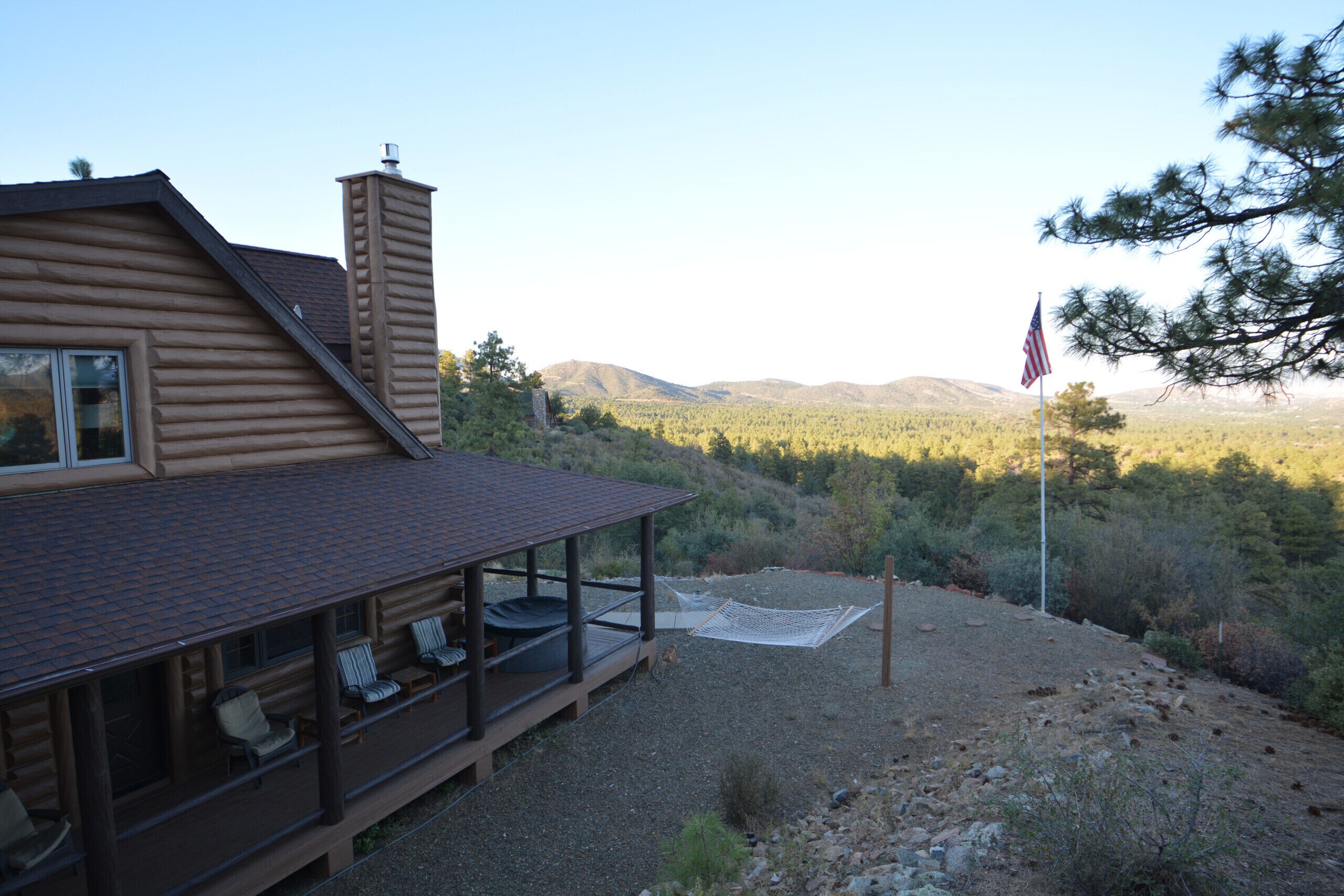 Une cabane en rondins dotée d’une véranda, d’un espace salon extérieur et offrant une vue sur un paysage montagneux.