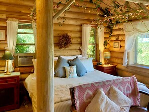 A cozy log cabin bedroom with a bed, bedside tables, and a window with curtains. - Log Cabin at Lynx Farm - Prescott Cabin Rentals (Prescott)