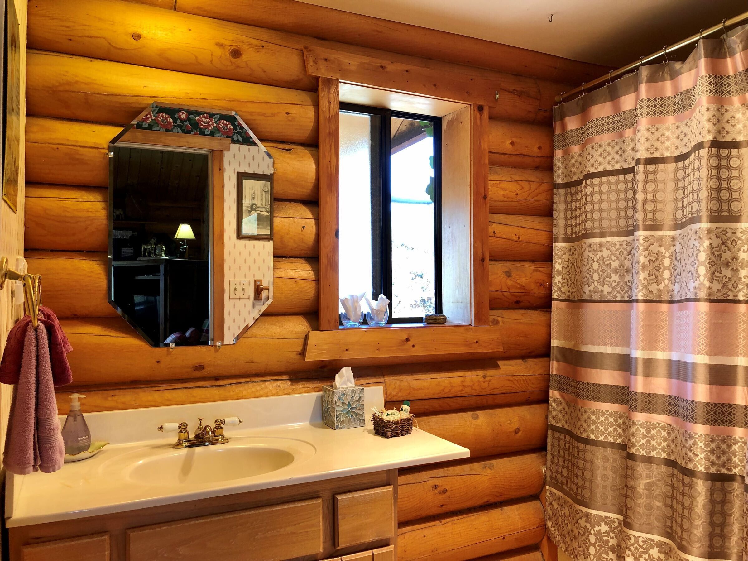A wooden cabin bathroom with a sink, mirror, window, and shower curtain.