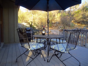 Une terrasse extérieure avec une table ronde, deux chaises, un barbecue et une bouteille de vin.