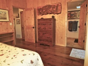 A room with wooden walls, a bed with floral bedding, a dresser with multiple drawers, and a door leading to another room.