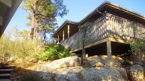 En tvåvånings stuga byggd av trä, med en balkong, belägen på en bergssluttning omgiven av träd.