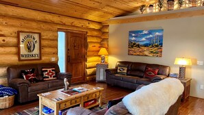 A log cabin interior with a wooden ceiling, a fireplace, a sofa, a coffee table, and a painting of a desert landscape. - Timbertrail Lodge - Prescott Cabin Rentals (Prescott)