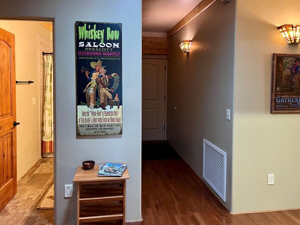 A hallway with a poster of a saloon, a wooden door, a light fixture, and a framed picture on the wall. - Timbertrail Lodge - Prescott Cabin Rentals (Prescott)
