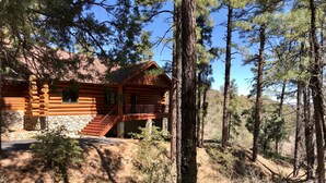 A log cabin with a stone foundation, a wooden deck, and a staircase leading to a porch. - Timbertrail Lodge - Prescott Cabin Rentals (Prescott)
