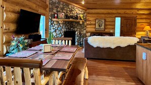 A log cabin interior with a stone fireplace, wooden furniture, a television, and a ceiling fan. - Timbertrail Lodge - Prescott Cabin Rentals (Prescott)