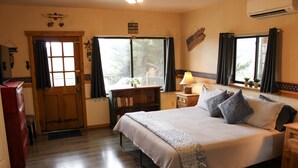 A bedroom with a large bed, a wooden dresser, a nightstand with a lamp, a bookshelf, and a window with curtains. - Liberty & Sunflower Suite - Prescott Cabin Rentals (Prescott)