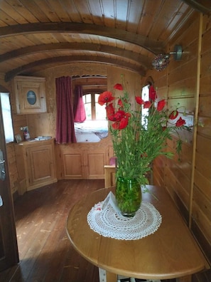 A wooden interior with a round table, a vase with red flowers, and a window with a view. - Comfortable self-catering caravan (Léognan)