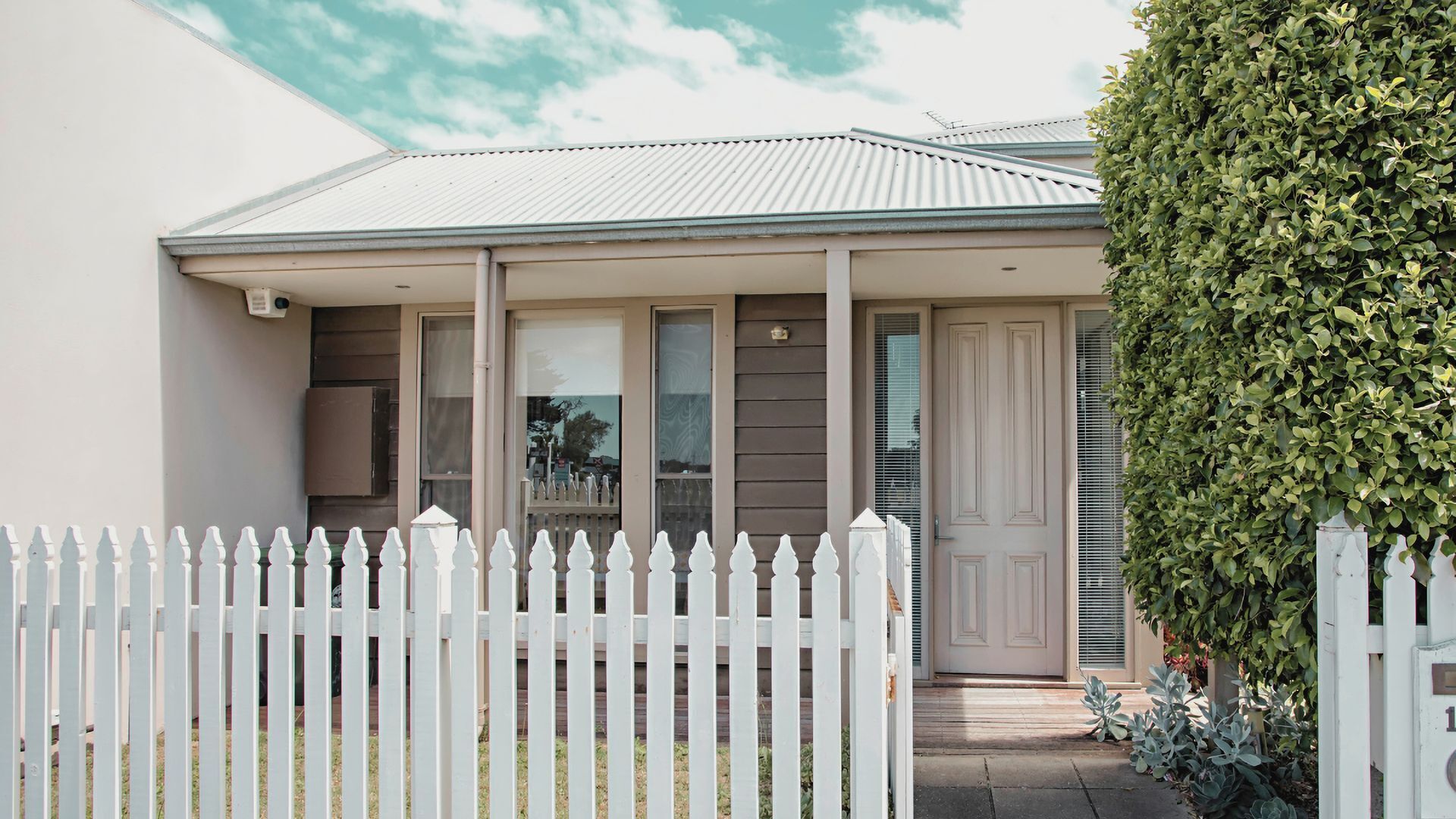 A residential house with a front porch, a picket fence, and a well-maintained hedge.