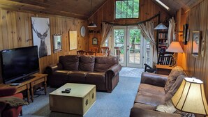 A cozy cabin interior with a wooden ceiling, a large TV, leather sofas, and a dining area with a view of the outdoors. - Dandelion's Lair, a 3 bedroom, 2.5 bathroom cabin in Twain Harte! (Twain Harte)