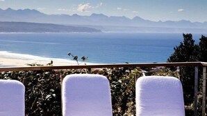 A seaside view with a balcony, chairs, and a distant mountain range. - Stella Maris (Plettenberg Bay)