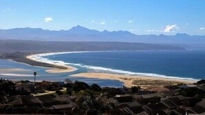 A coastal landscape with a beach, ocean, and mountains in the background. - Stella Maris (Plettenberg Bay)