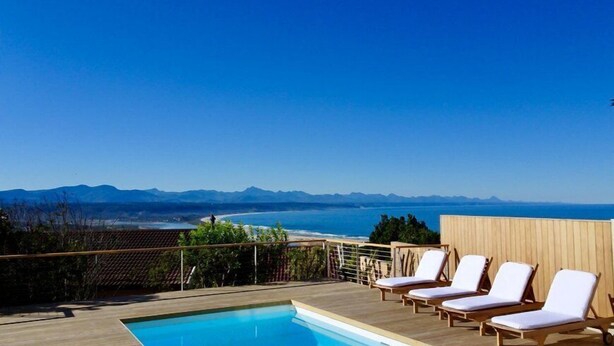 A poolside area with lounge chairs and a view of the ocean and mountains. - Stella Maris (Plettenberg Bay)