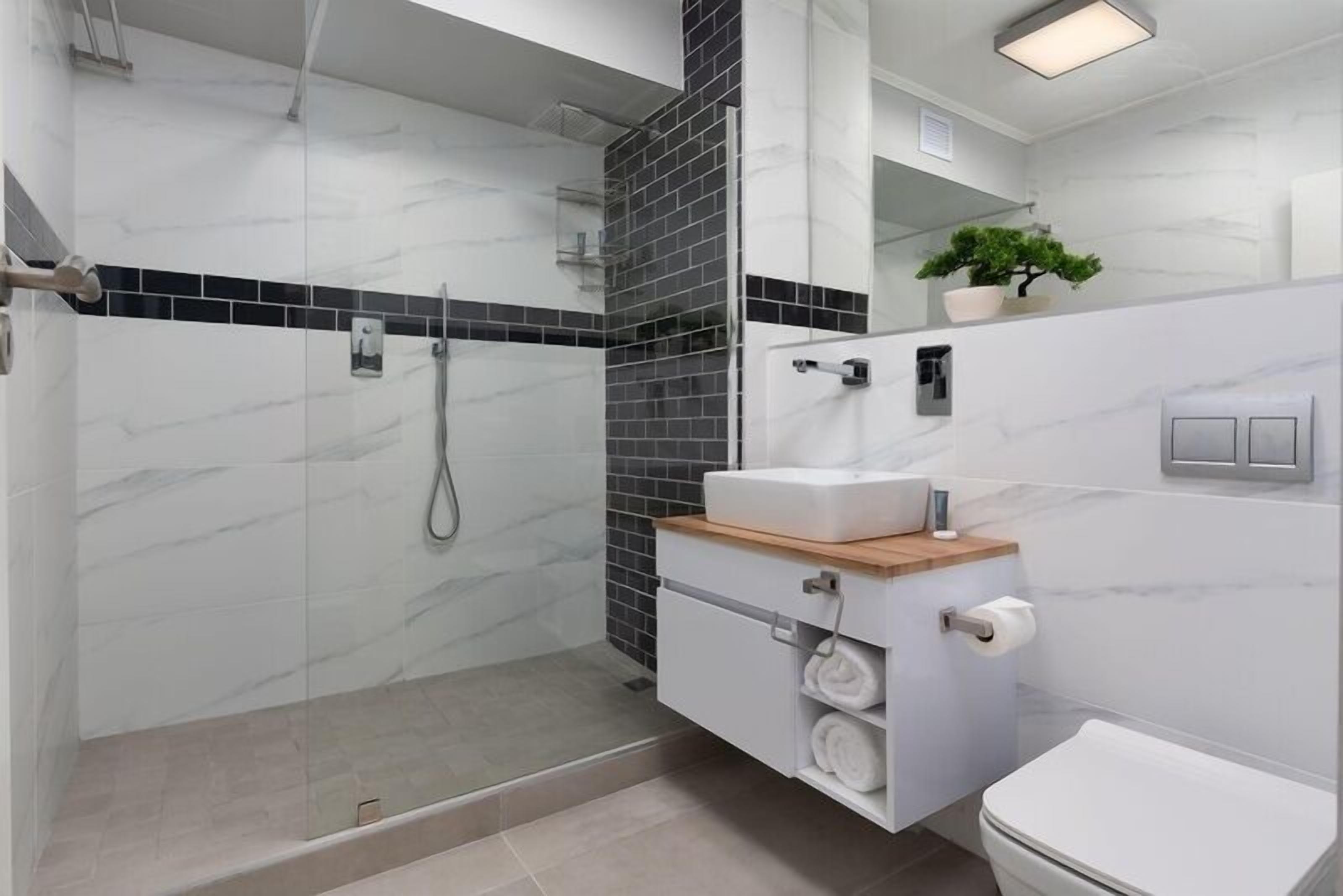 A modern bathroom with a glass-enclosed shower, a white sink with a wooden countertop, and a toilet.