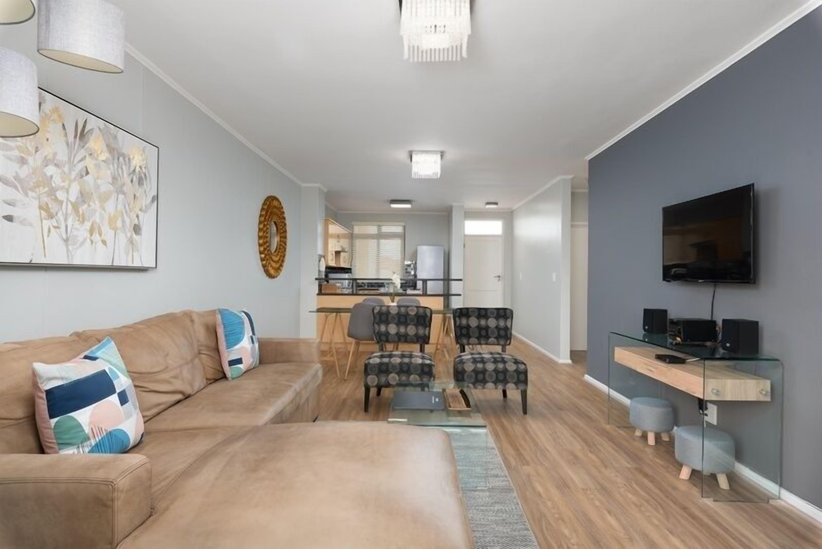 A modern living room with a sofa, chairs, a coffee table, and a TV. There is a kitchen in the background.