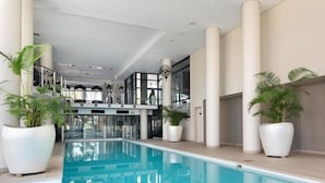 Een binnenzwembad met witte kolommen, potplanten en een modern architectonisch ontwerp.