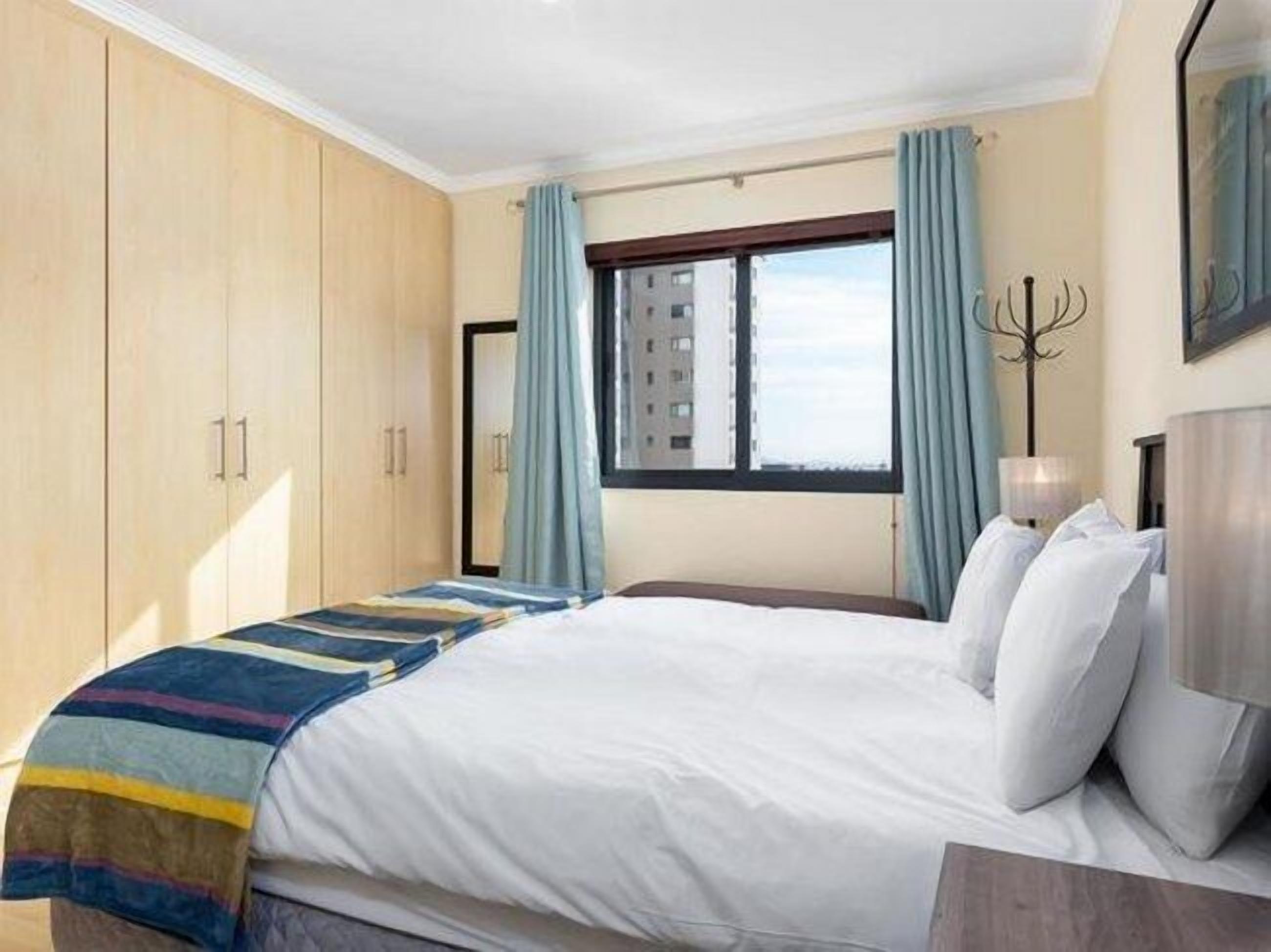 Een hotelkamer met een groot bed, een kledingkast, een raam met gordijnen en uitzicht op een gebouw.