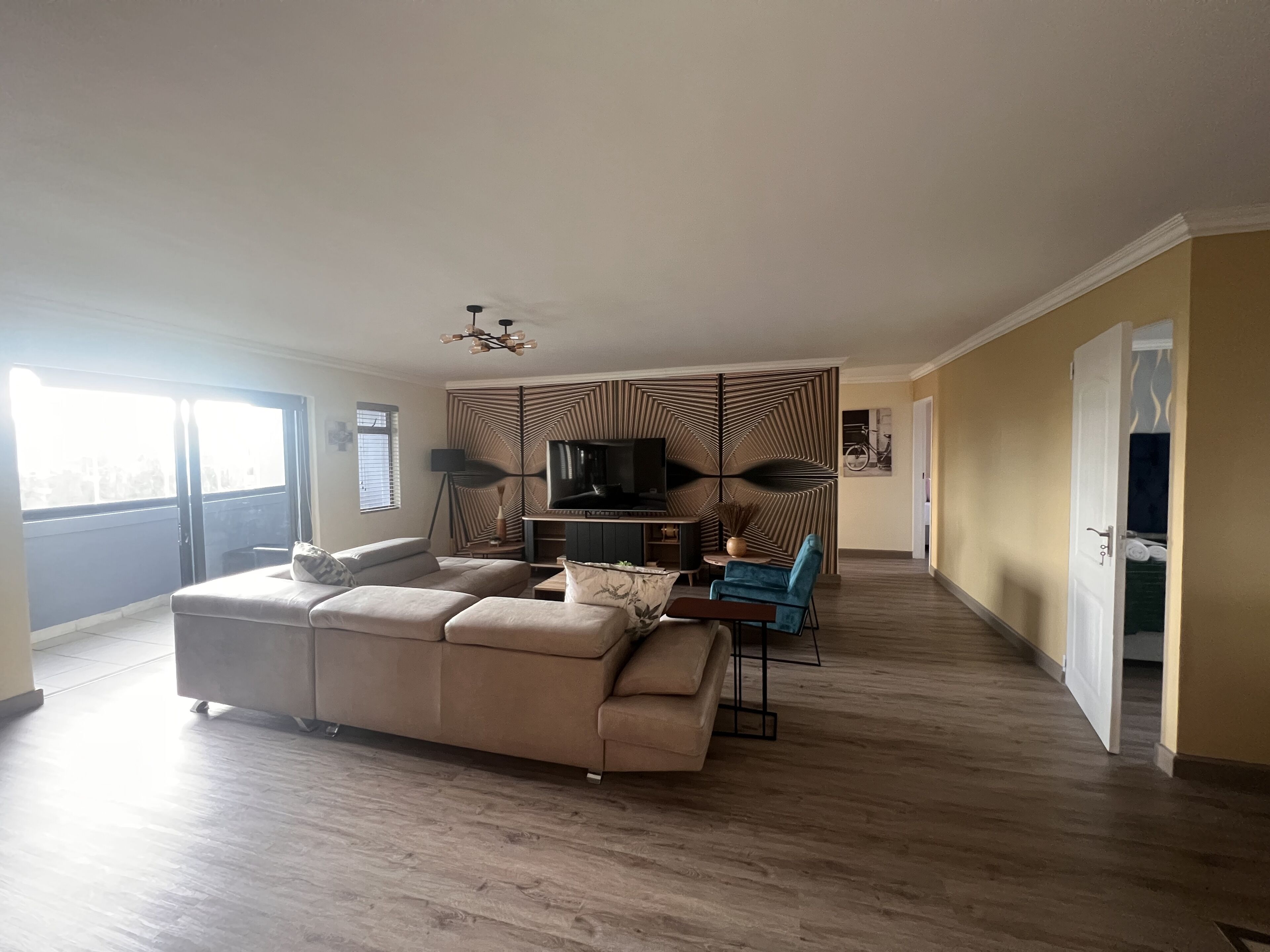 A spacious living room with a large sofa, a TV, and a decorative wall panel.