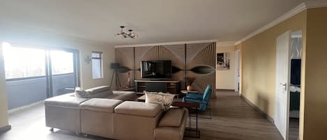 A spacious living room with a large sofa, a TV, and a decorative wall panel.