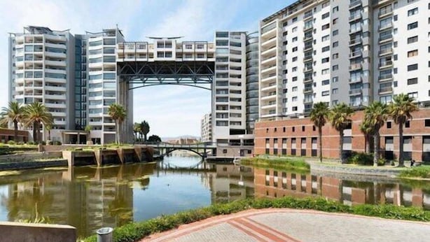 Een modern wooncomplex met hoge gebouwen, een centrale boog en een waterpartij.