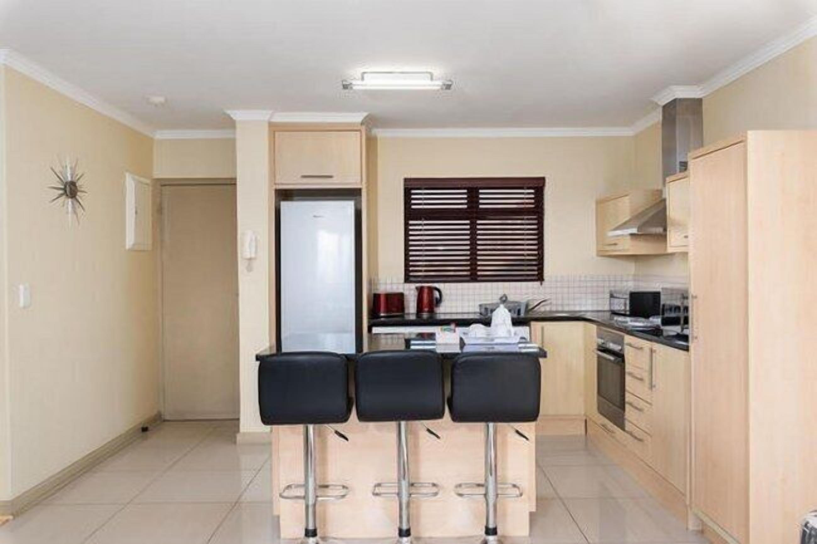 Cocina compacta con refrigerador, estufa y pequeño comedor con tres taburetes.
