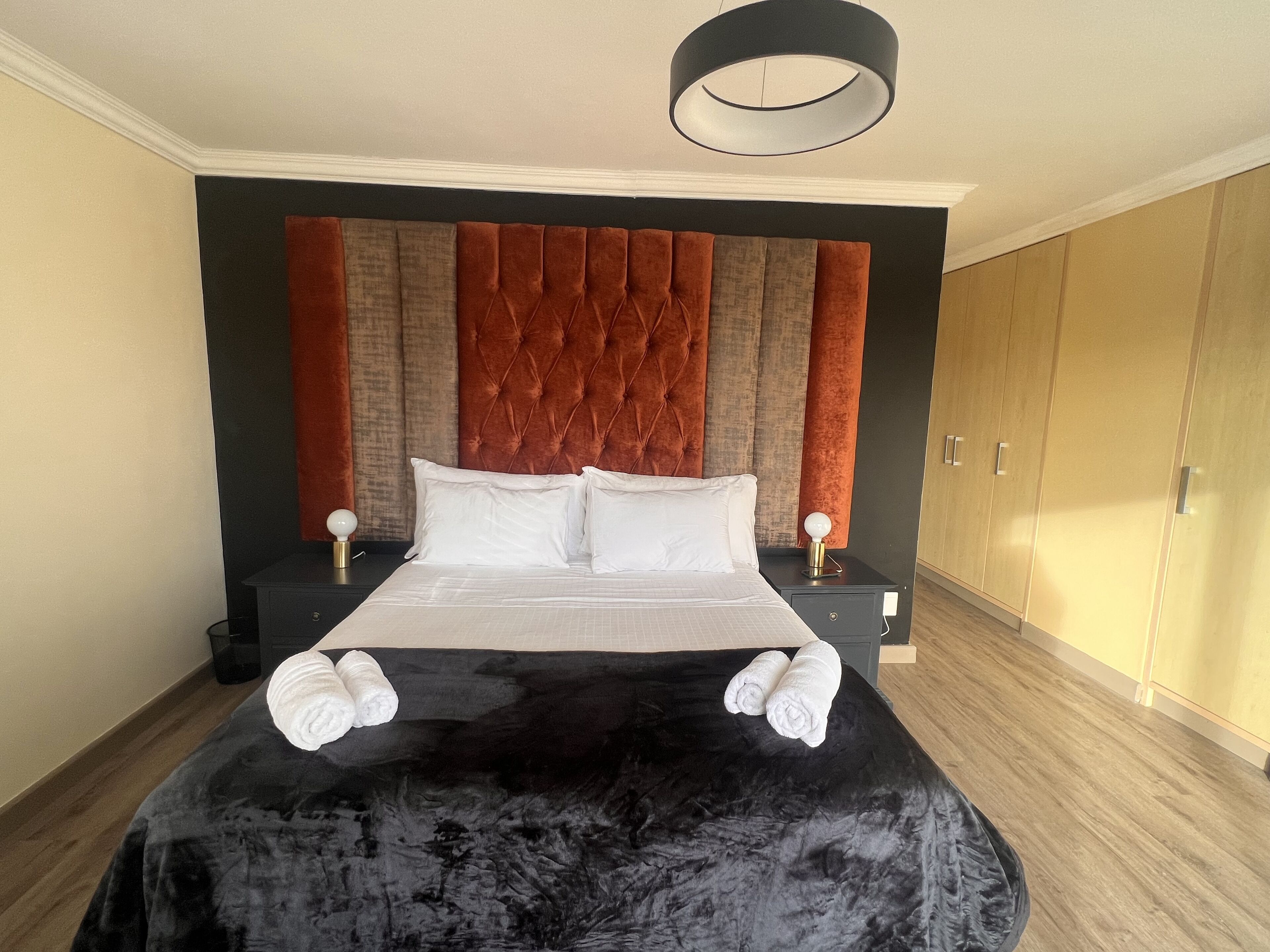A neatly made bed with white linens and towels, a tufted headboard, and a modern pendant light.