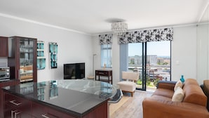 Een moderne keuken met een centraal eiland, een zithoek met een bank en een groot raam met uitzicht op de stad.