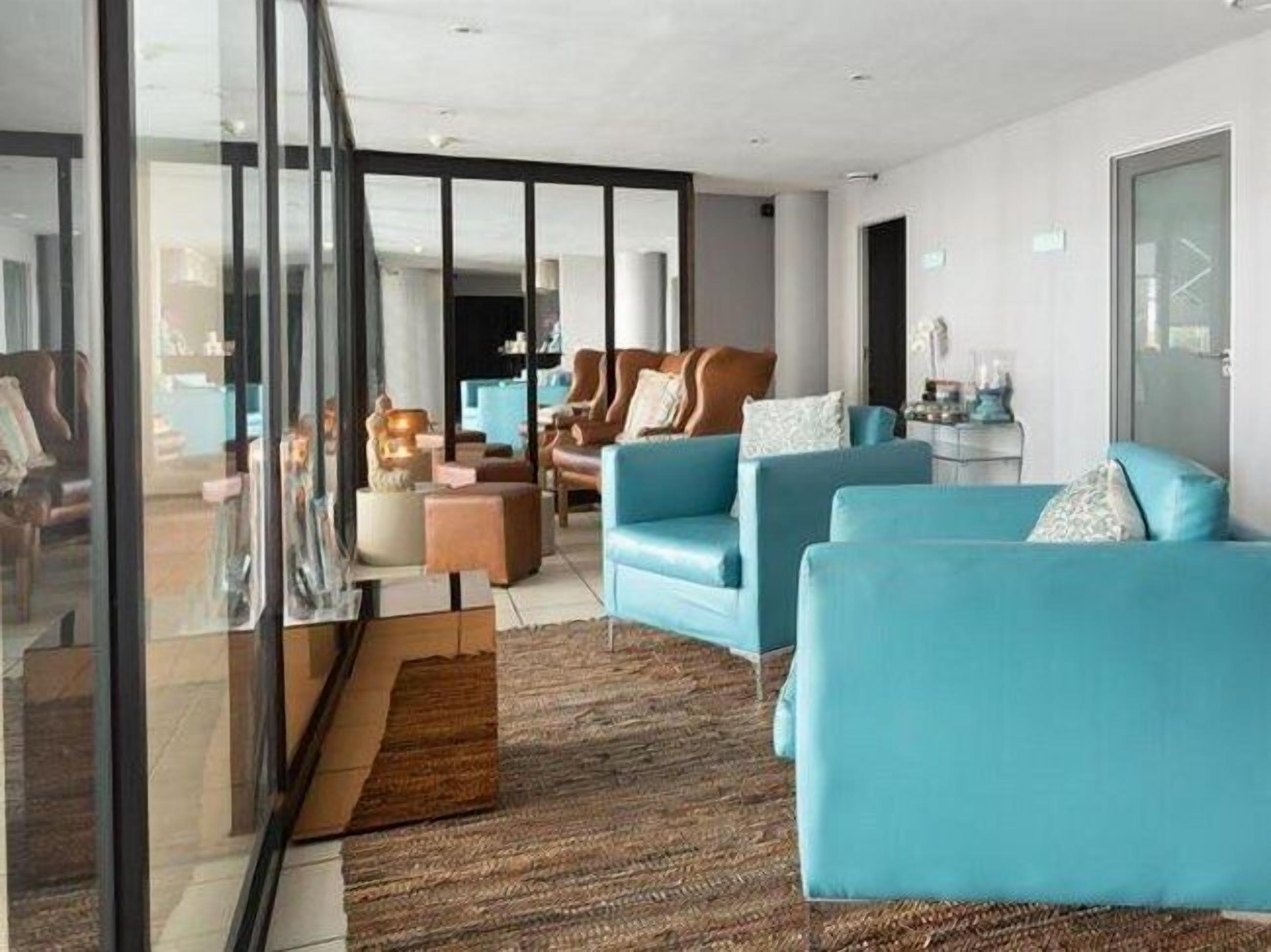 Una sala de estar moderna con una pared de vidrio, un sofá azul, un sillón marrón y una alfombra estampada.