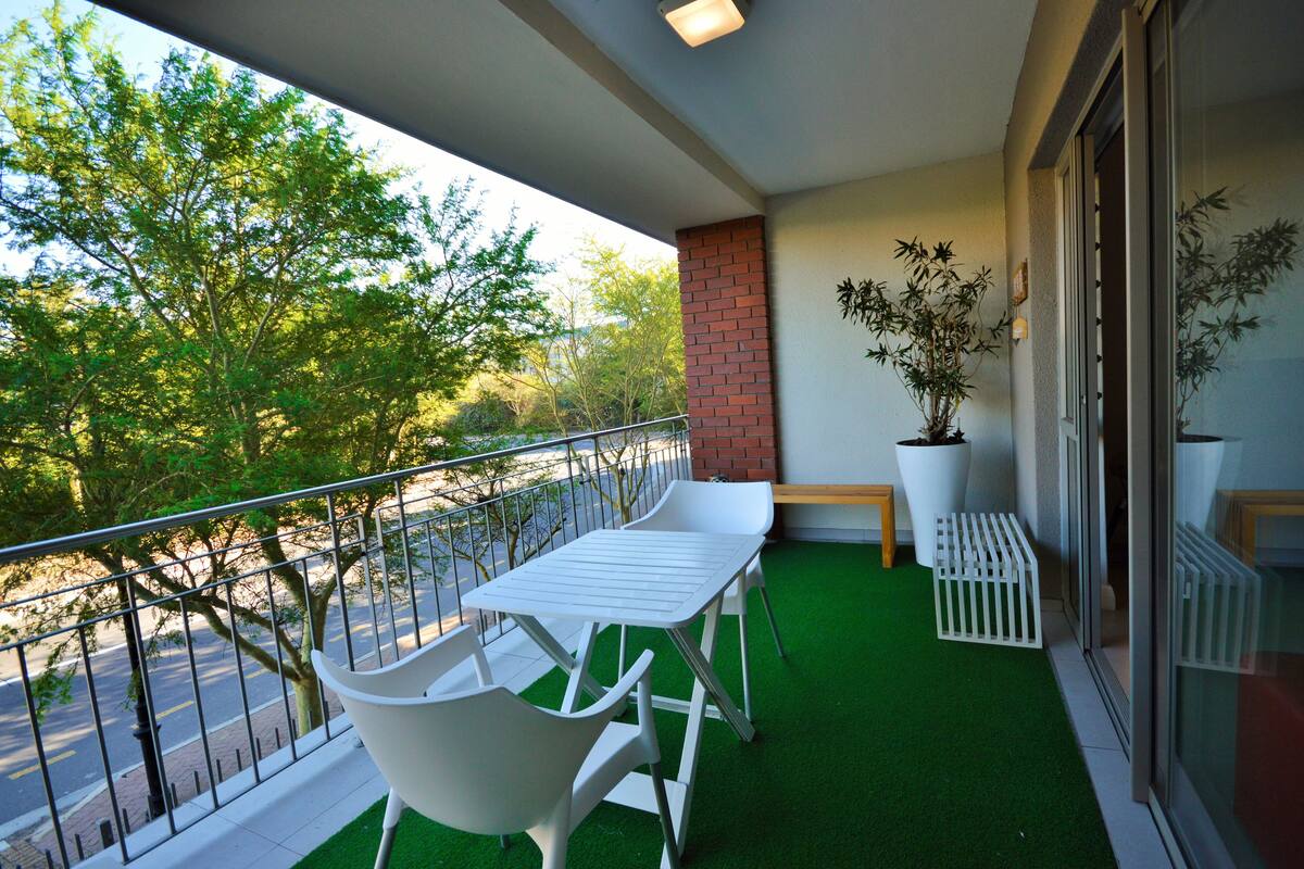 A balcony with a white table and chairs, green artificial turf, and potted plants.