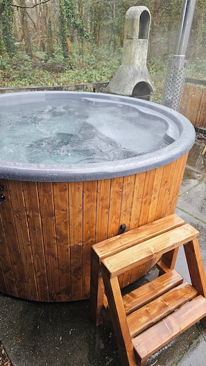 A wooden hot tub with a built-in bench, surrounded by a natural setting.