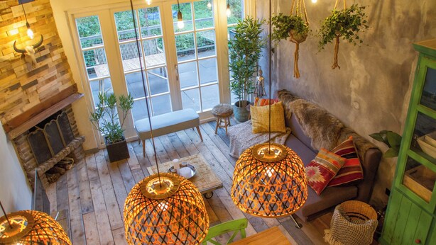 Una sala de estar acogedora con chimenea, suelo de madera y lámparas de mimbre colgantes.