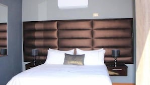 A modern hotel room with a large bed, a padded headboard, two bedside tables with lamps, and a small window above the bed.