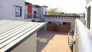 A residential building with a flat roof, a balcony, and a fenced backyard.