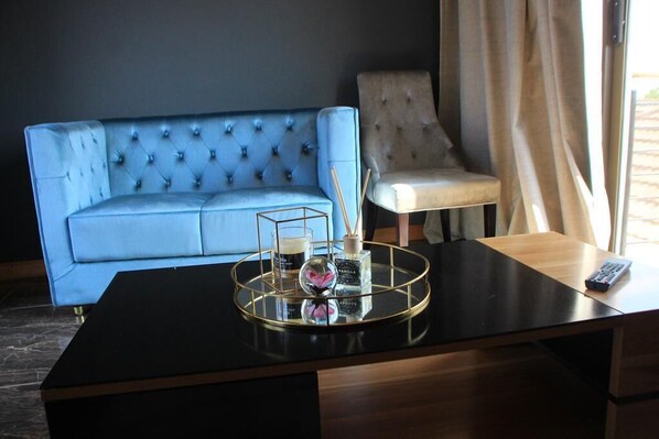A modern room with a dark blue sofa, a light-colored armchair, and a wooden desk with a tray holding a glass, a bottle, and a candle.