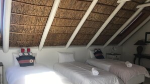 Ett rum med två sängar, ett halmtak och ett litet bord med en lampa.