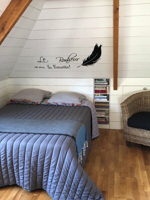 Une chambre confortable avec un lit, des oreillers, une bibliothèque et un fauteuil en osier.