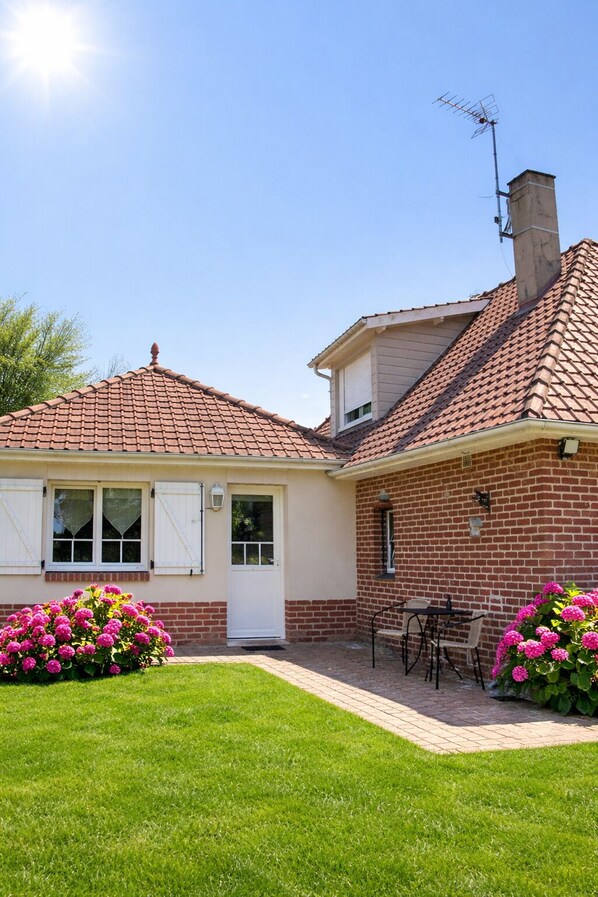 Une maison à deux étages, avec un toit en tuiles, une cheminée et un petit patio équipé d’une table et de chaises.