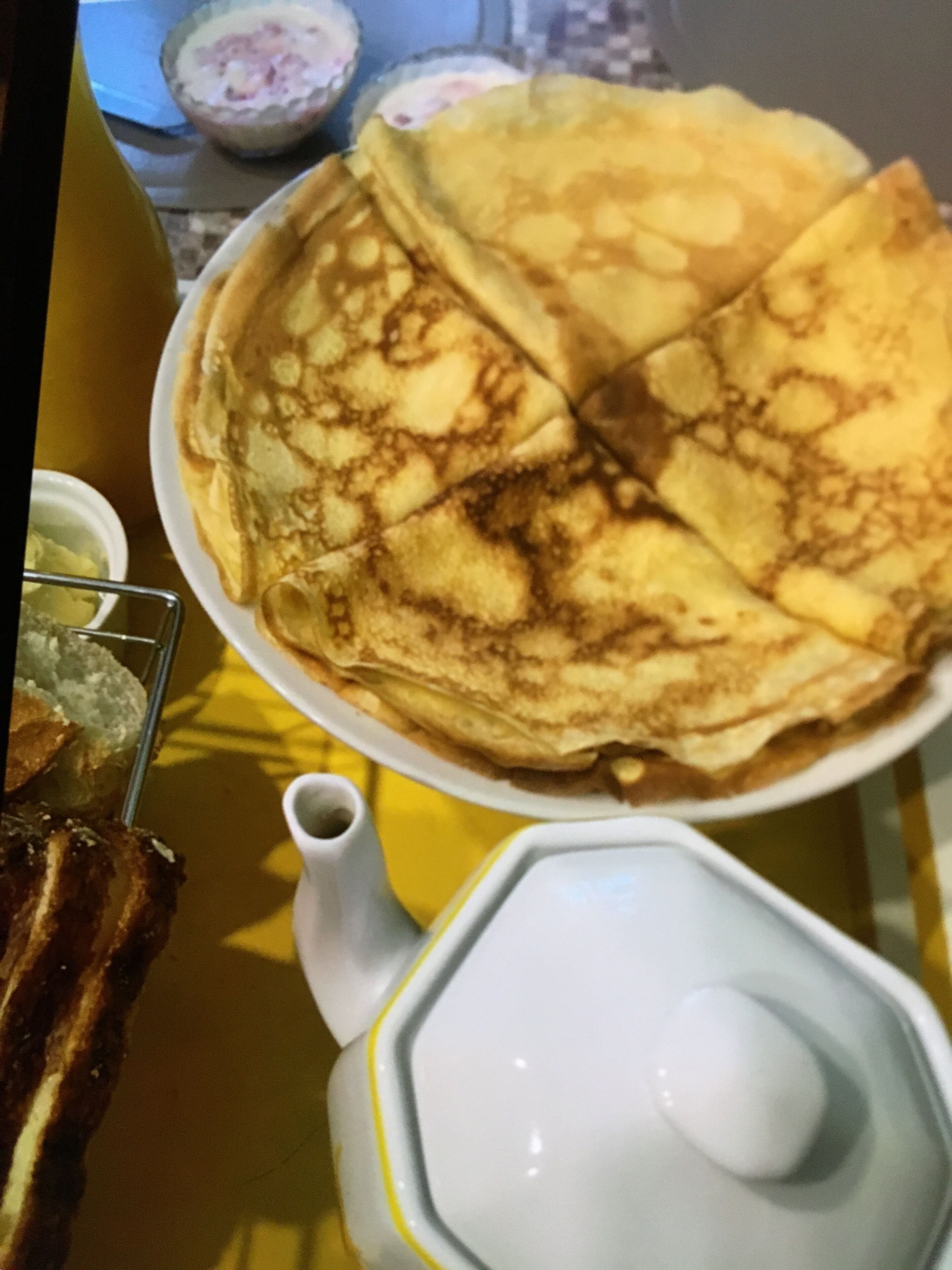 A plate of crepes with a white pitcher and a small bowl of syrup.