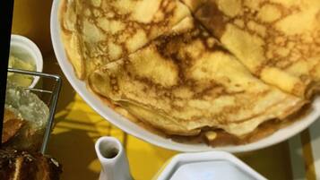 A plate of crepes with a white pitcher and a small bowl of syrup.