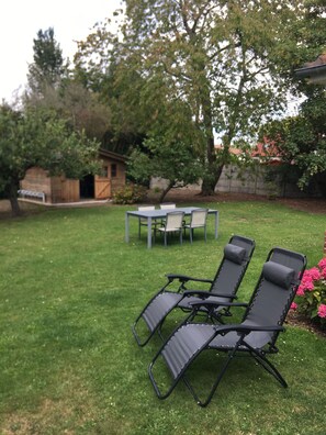 Un jardin avec une pelouse, une table et des chaises, et un petit abri de jardin.