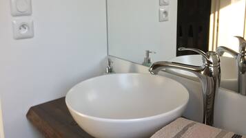 Ein Badezimmer mit einem weißen Waschbecken, einer Holzablage und einem Spiegel darüber.