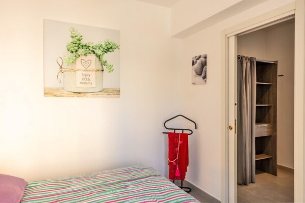 A bedroom with a bed, a wall-mounted plant, a red towel on a rack, and a closet with a curtain.