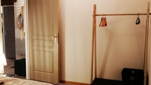 A bedroom with a bed, a wooden door, a hanging light fixture, and a coat rack with clothes and a suitcase.