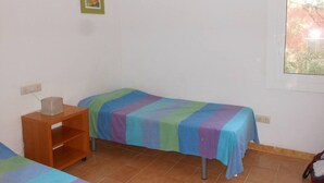 Una habitación pequeña y limpia con dos camas individuales, una mesita de noche de madera y una ventana con vistas a zonas verdes.