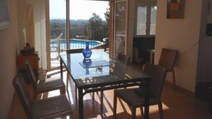 Un comedor con mesa y sillas de vidrio, un florero azul y vista a una piscina a través de amplias puertas de cristal.