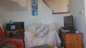 Un dormitorio con cama, televisión, escritorio con computadora y un cuadro en la pared.